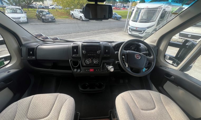 Cab and dashboard of the 2017 Auto-Trail Tribute 625 motorhome showing driver and passenger seats with controls and steering wheel.