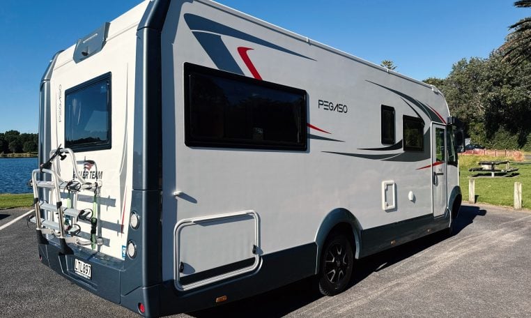 2018 Roller Team Pegaso 745 exterior showing the rear driver's side and bike rack next to a lakeside.