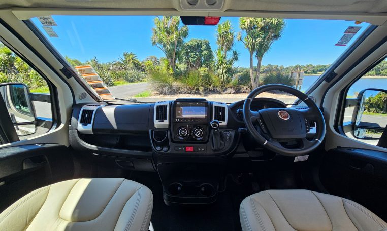 Cab and dashboard of the Auto-Trail Frontier Comanche motorhome showing driver and passenger seats with controls and steering wheel.